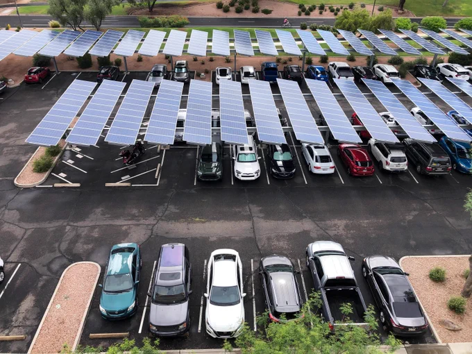 A parking lot with multiple rows of cars parked under large solar panel canopies providing shade and renewable energy.