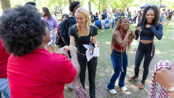 A group of people are outdoors on the Horseshoe, smiling and holding cords being distributed by a person in a red shirt. Other attendees and event booths are visible in the background.