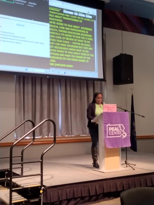 Photo of DRP staff attorney, Jenee Oliver, presenting on stage behind a purple podium that says PEAL Center on it. 