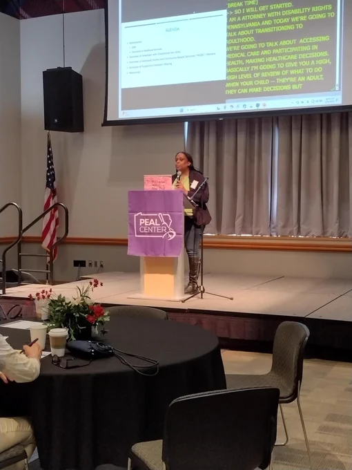 Photo of DRP staff attorney, Jenee Oliver, presenting on stage behind a purple podium that says PEAL Center on it. 