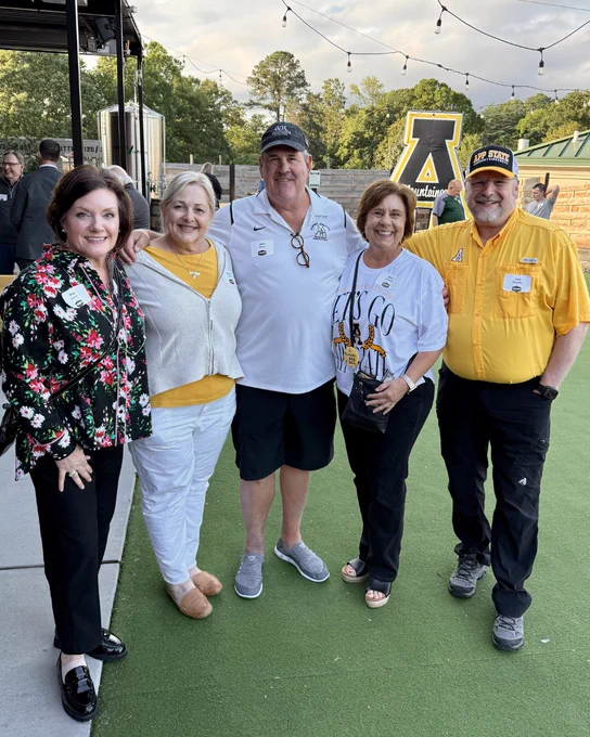 Group of Mountaineers smiling together outdoors at a Mountaineer Spring Tour stop with an App State block A sign in the background.