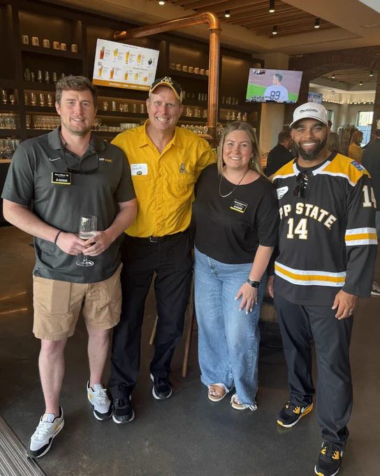 Mountaineers posing together inside a brewery during a Mountaineer Spring Tour event with App State apparel and drinks.