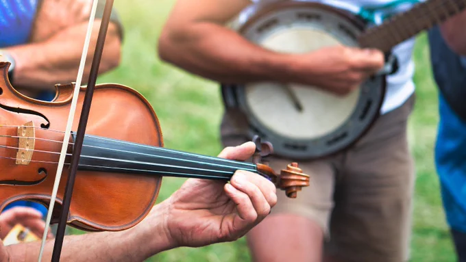 Image close-up of individuals playing a violin and a banjo outdoors.