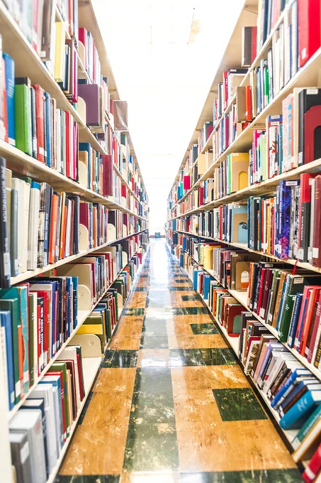 A brightly lit library aisle with tall shelves filled with colorful books on both sides.