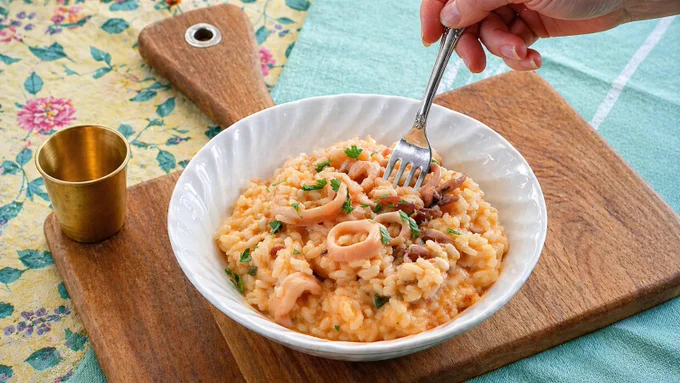 Serving creamy seafood risotto in a white bowl with a fork.