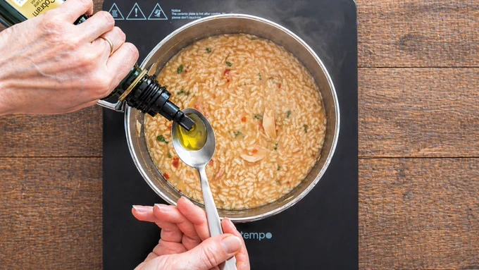 Adding olive oil to risotto in a pot on an induction cooktop.