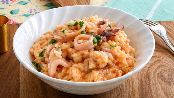 Close-up of creamy seafood risotto with squid and parsley in a bowl.