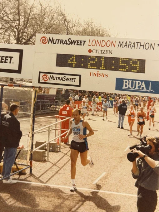 Annie's dad, Steve, crossing the finish line of the NutraSweet London Marathon, with a time of 4:21:59 displayed above. Other participants are visible in the background.