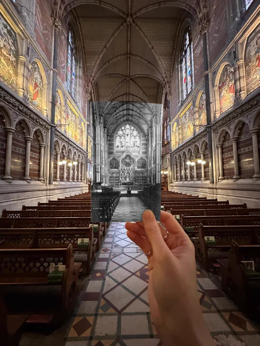Inside Keble Chapel, a hand holds a historic black-and-white photo aligned with the modern interior, showing rows of wooden pews, patterned floor tiles, and ornate arches leading to the altar.
