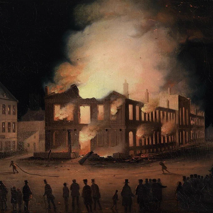 Night scene of a large stone building engulfed in flames, with fire pouring from windows and roof. Thick smoke rises high into the dark sky, glowing orange from the blaze. The structure’s walls are partially collapsed, exposing interior beams. A crowd of people in 19th-century clothing stands in the foreground watching, many wearing hats and long coats. A few figures move closer to the fire, one holding a hose, while nearby buildings remain intact but dimly lit by the glow.
