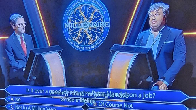 The image displays a screenshot from a satirical comedy sketch titled **"Who Wants to Remain a Millionaire,"** parodying the famous game show format. Two men are positioned behind glowing, high-tech podiums in a dark studio setting illuminated by blue and yellow neon accents. The man on the left, acting as the host, wears a formal dark suit and glasses, while the man on the right, the "millionaire" contestant, appears disheveled with messy hair and an open-collared suit. A large blue graphic at the bottom presents a humorous, biased multiple-choice question: **"Is it ever a good idea to give Peter Mandelson a job?"** with the options being **"No,"** **"Of Course Not,"** and **"Not In A Million Years."** White subtitles capture the contestant’s mock-serious dilemma as he says, **"Jeremy, I think I'm going to have to use a lifeline."**