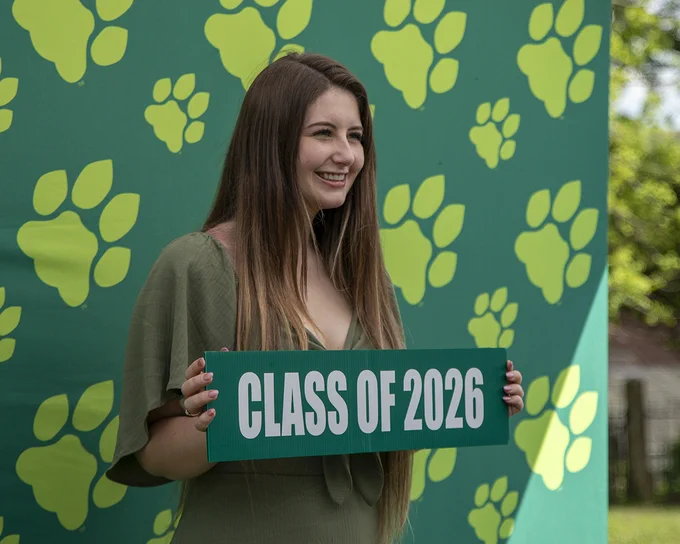 Person holding a Class of 2026 sign in front of a paw print backdrop in a photo booth