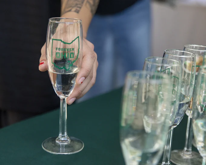 Hand holding a champagne flute with a Forever OHIO logo on it