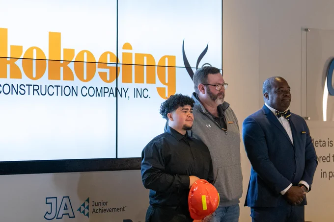 A student holding a hardhat poses with two men after signing with the construction company Kokosing during CTE Signing Day. 