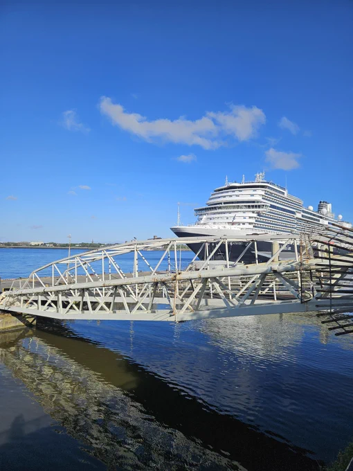 Cruise ship on the River Mersey; blue sky with some cloud; reflection of ship in the water; metal structure in front of ship