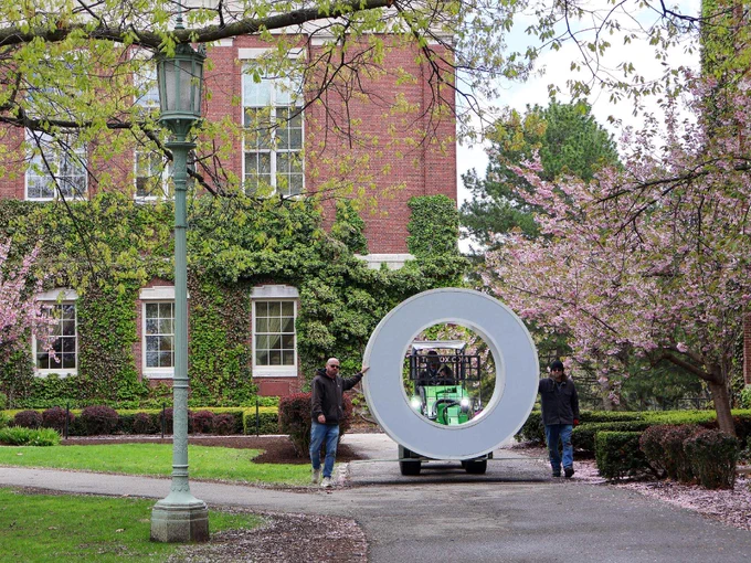 Two grounds keepers navigate a giant letter O on a forklift across the quad, past the cherry trees. 