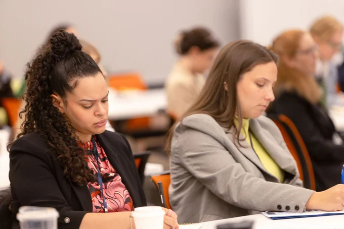 A photo of two women taking notes in a conference room