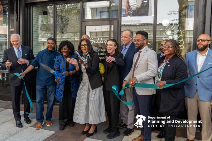 Many people celebrating in front of a store holding a teal ribbon that is cut.
