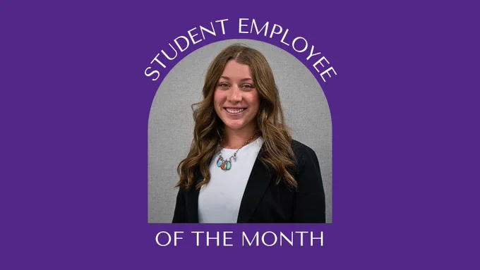 A person with long hair is smiling, wearing a blazer and white shirt, standing in front of a gray background. The text above reads "Student Employee" and below "Of the Month," on a purple backdrop.
