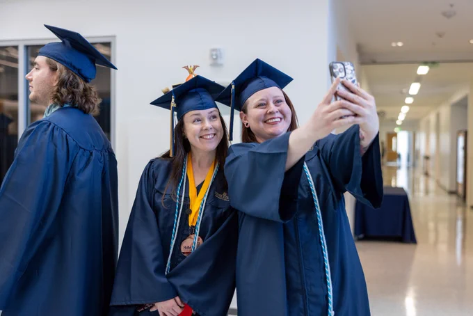 Two female graduates pose for a selfie in their cap and gown.