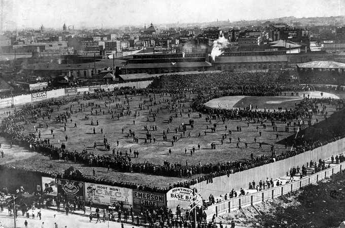 Monochrome, high-angle shot of a baseball field filled with people; more crowd around the perimeter.