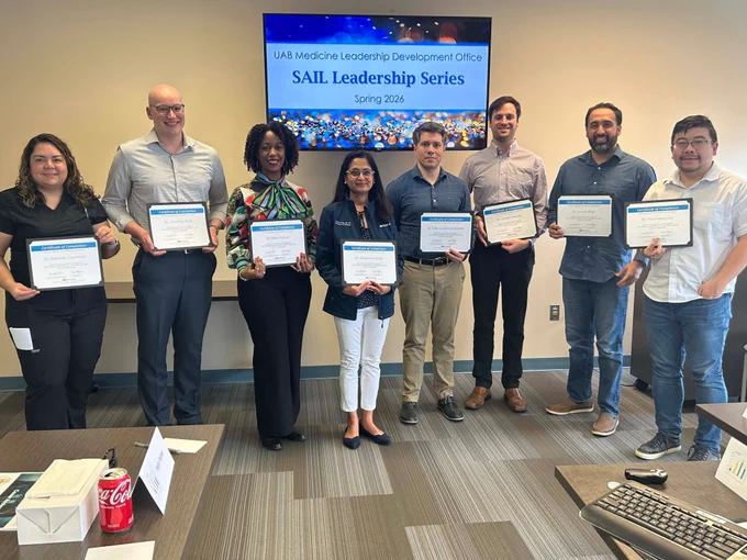 A group of people stand in a line holding diplomas.