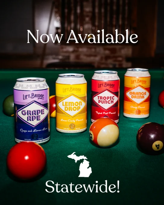 An image showcasing four Lift Bridge beverage cans placed on a pool table with billiard balls. The drinks are now available statewide, as indicated by the text and map of Michigan.