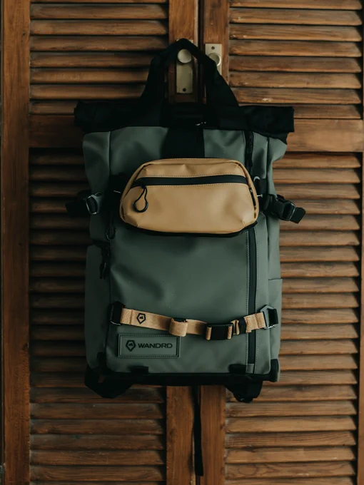 A sleek backpack with a light brown front pocket hung on a wooden door with slated panels. The setup gives a rustic and adventurous feel.
