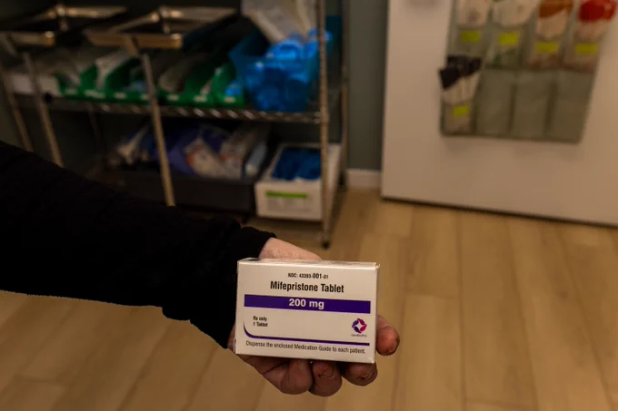 Box of mifepristone being held by hand over a wooden floor. 