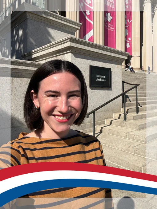 Caroline in a gold with black stripes top smiling in front of the National Archives building