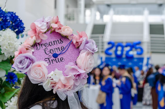 A pink graduation cap with flowers around the edge and the words: dreams come true.
