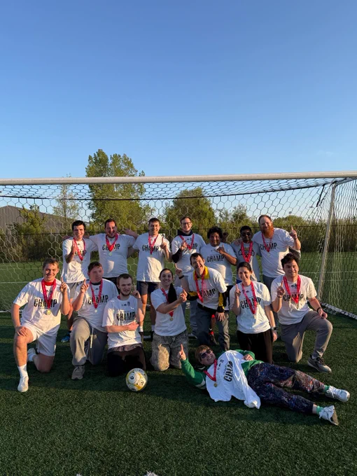 A soccer team gathered together in a goal, wearing matching champion shirts and medals.