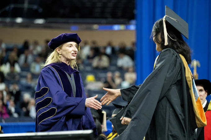 Sharon F. Matusik, Edward J. Frey Dean of Business, shakes hands with a student wearing a graduation cap and gown.
