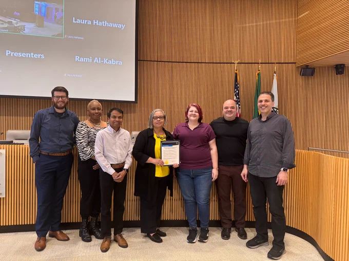 AC Petersen from the Bothell Arts Commission stands with Bothell City councilmembers in Council Chambers inside Bothell City Hall. AC is holding a proclamation. 
