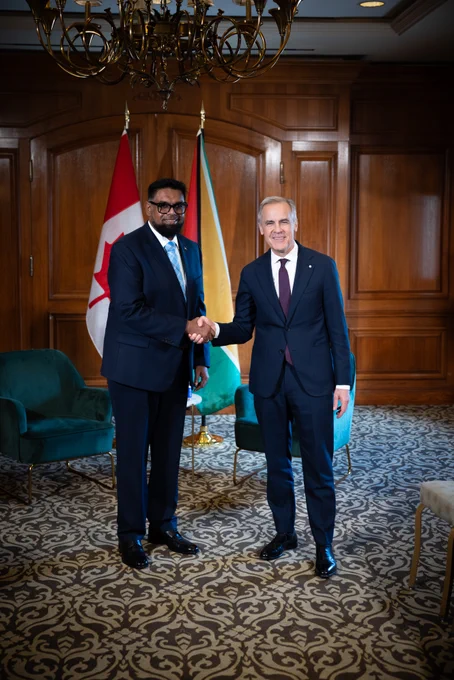 Prime Minister Mark Carney is shaking hands with the President of Guyana, Dr. Mohamed Irfaan Ali. The flags of Canada and Guyana are situated behind them.
