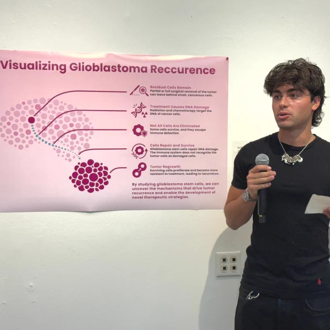 A person is speaking into a microphone while standing next to a poster titled "Visualizing Glioblastoma Recurrence." The poster features a diagram with labeled sections about cancer cells and treatment effects.