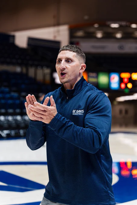 UC Davis strength coach mid-clap prior to a basketball game standing on the court.