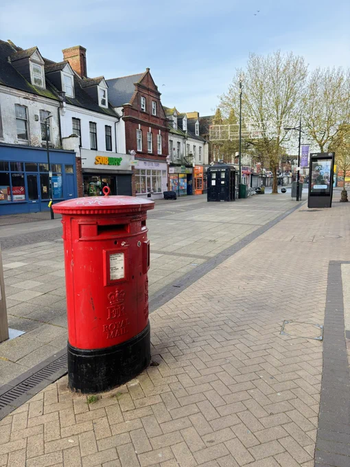 A pedestrian street, a double red phone box in the foreground, shops and building in the background.