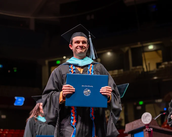 Boise State graduate students walking across the stage after receiving their masters diploma. 

