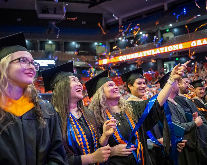 Boise State graduate students watching streamers fall to the floor at the Spring 2026 commencement ceremony. 

