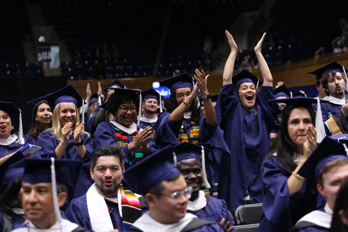 Students wearing graduation caps and gowns cheer. 
