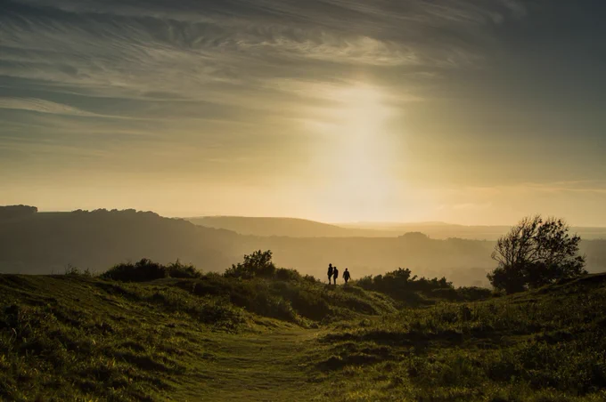 Three silhouettes of walkers in the distance captured in a warm evening light at Cissbury Ring.