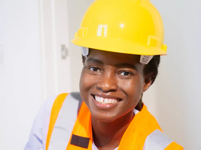 Close-up of a smiling female engineer wearing protective gear indoors.