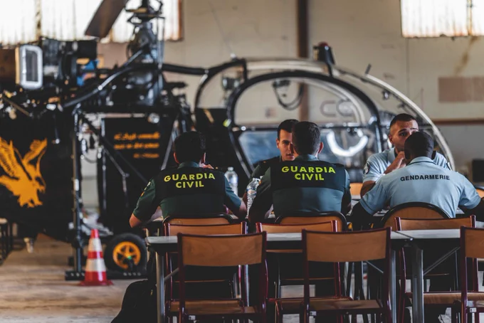 Photographies de policiers Espagnols et de gendarmes Français assis autour de la même table. On voit un hélicoptère en fond.