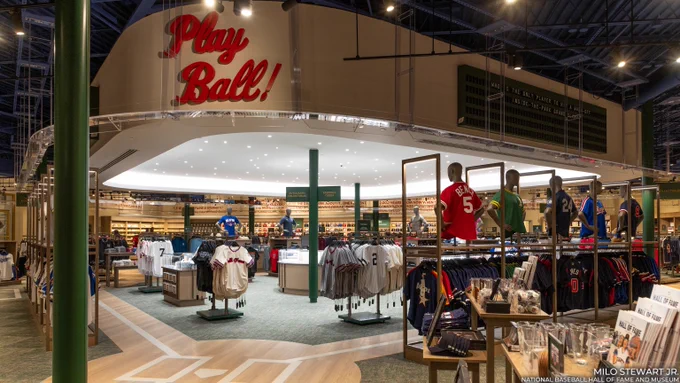 General view of the Museum store with baseball jerseys, caps and gear displayed under a large sign with Play Ball written in red script. (Milo Stewart Jr./National Baseball Hall of Fame and Museum)