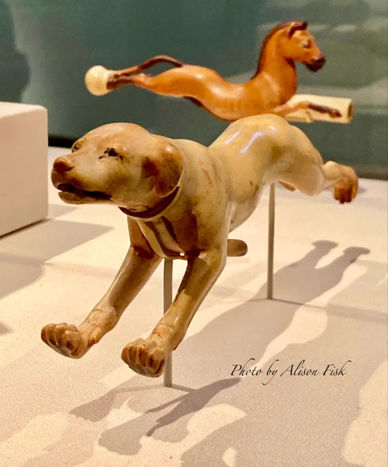 My photo shows a three quarter left profile of an ancient Egyptian figurine of a leaping dog. Carved from ivory, now a warm caramel brown colour with glossy surface. The dogs eyes are outlined in black, the ears are floppy, the mouth is slightly ajar (the inside of the mouth is painted red - not seen in my photo). The front and back legs are outstretched as if running at full speed. A lever under the dog’s chest opens and closes the mouth so that the dog looks as if it’s barking. Dimensions: L 18.2 cm × H 6.1 cm × W 3.6 cm. Dated to Late Dynasty I8, I400-I350 BC, reign of Amenhotep III who was Tutankhamun’s grandfather.

The dog is mounted on a thin metal rod in a display case. In the background in the same display case is a ‘galloping’ brown horse, which is the handle of an ancient Egyptian fly whisk or light whip.