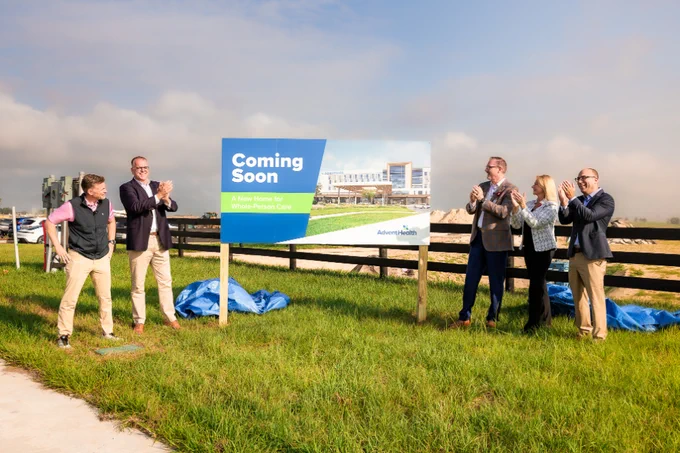 A group of professionals celebrate the announcement of a new facility with a 'Coming Soon' sign on a construction site.