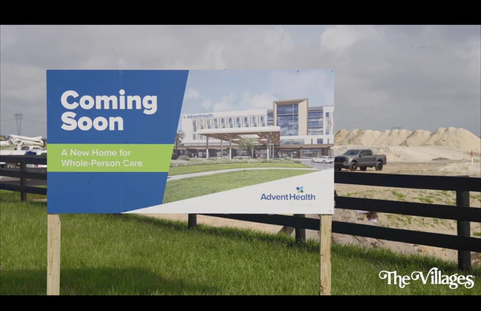 A sign announcing the upcoming construction of an AdventHealth facility, placed in a grassy area with a construction site in the background. The mood conveys anticipation and development.