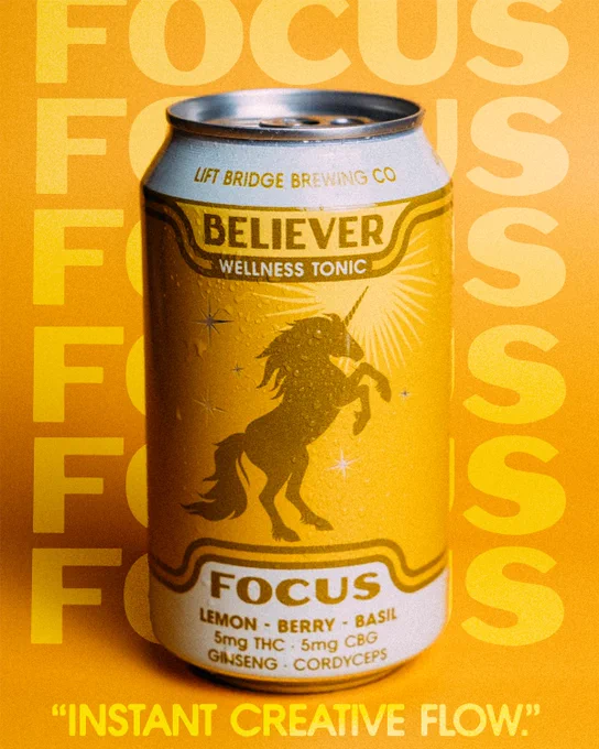 A vibrant yellow can labeled 'Believer Wellness Tonic' featuring a unicorn design against a repeated 'FOCUS' backdrop. The product includes ingredients like lemon, berry, basil, and 5mg each of THC and CBG.