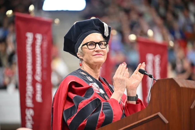 Color indoor photo of W S U President Cantwell clapping while at a lectern. 